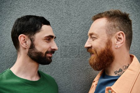 Foto de Pareja gay en casual atuendo stand juntos, mostrando amor y afecto contra un gris pared telón de fondo. - Imagen libre de derechos