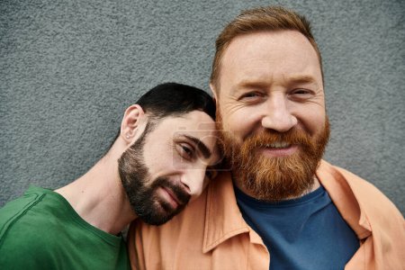 Foto de A gay couple in casual attire standing together against a grey wall in a portrait of love and solidarity. - Imagen libre de derechos