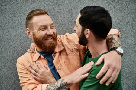 Téléchargez les photos : A portrait of a gay couple in love, wearing casual attire, embracing each other in front of a grey wall. - en image libre de droit