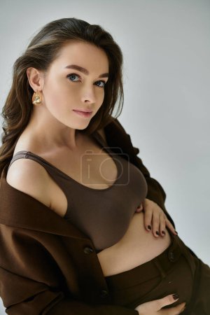 Une jeune femme enceinte exsudant grâce et chaleur dans une chemise brune pose pour un portrait.