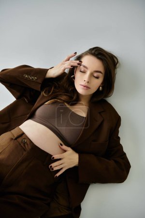 A young pregnant woman in a brown suit leans against a wall .