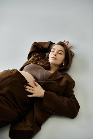 A young pregnant woman in a brown suit with a blazer is peacefully laying down on the floor.