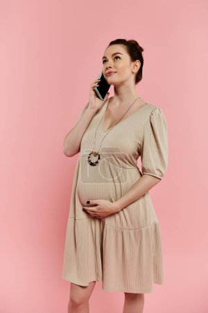 Eine stilvolle schwangere Frau in einem Kleid plaudert auf einem Handy vor einem leuchtend rosa Hintergrund.