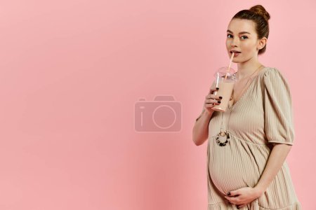 Foto de A young pregnant woman in a dress holding milkshake on a pink background. - Imagen libre de derechos