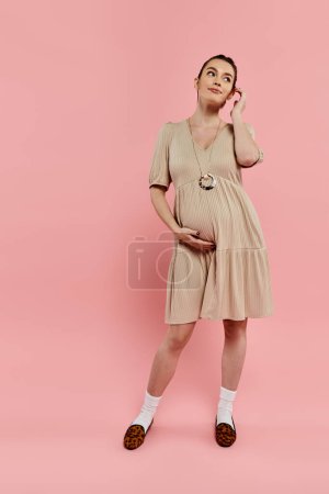 Foto de Una mujer embarazada radiante de pie con gracia delante de un fondo rosa. - Imagen libre de derechos