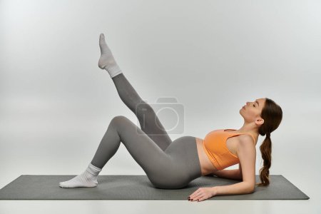 Photo for A young, sporty pregnant woman gracefully practices yoga on a mat against a grey background. - Royalty Free Image