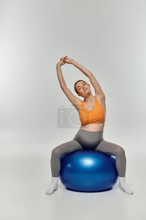Sportliche Schwangere balanciert in aktiver Kleidung auf einem knallblauen Gymnastikball.