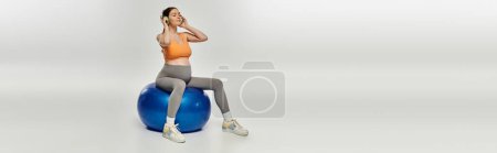 A pregnant woman in activewear sits gracefully on a blue exercise ball, showcasing strength and balance.