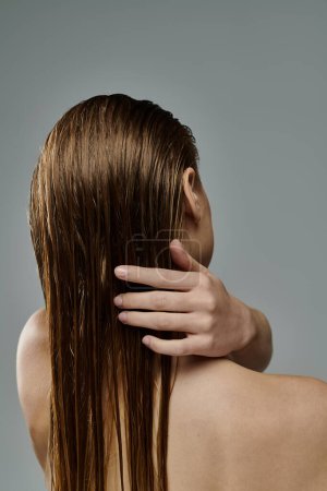 Appealing woman with long hair is gently touching her wet hair.