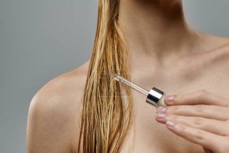 Téléchargez les photos : Attractive woman holding a hair serum, displaying her hair care routine with wet hair. - en image libre de droit