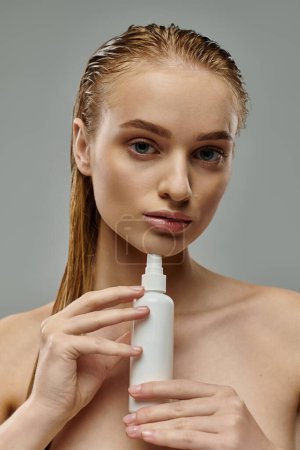 Photo for A young, beautiful woman holding a bottle of lotion, tending to her hair. - Royalty Free Image