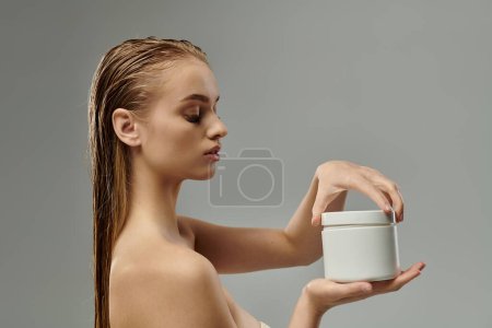 Téléchargez les photos : Une jeune belle femme présentant sa routine de soins capillaires avec les cheveux mouillés, tenant un récipient. - en image libre de droit