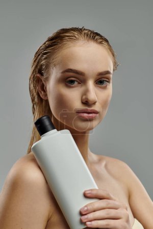 A young woman showcases her hair care routine holding a bottle of shampoo.