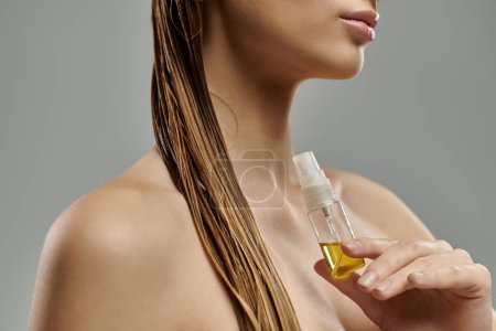 Eine junge Frau hält eine Flasche Öl in der Hand und zeigt ihre Haarpflege-Routine mit nassen Haaren.