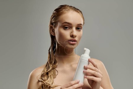 Téléchargez les photos : Une jeune femme aux cheveux mouillés tient une bouteille de lotion dans ses mains, mettant en valeur sa routine de soins capillaires. - en image libre de droit