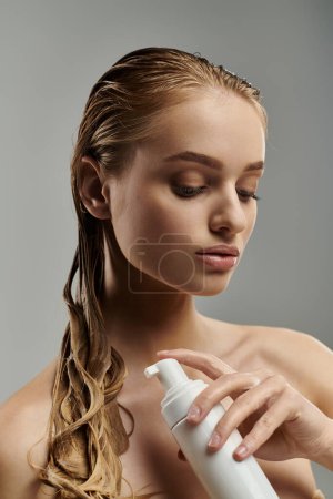 Attractive woman with wet hair holds a bottle of lotion in her hands, showcasing her hair care routine.