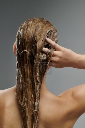 Photo for A young beautiful woman demonstrates her hair care routine, washing her hair. - Royalty Free Image