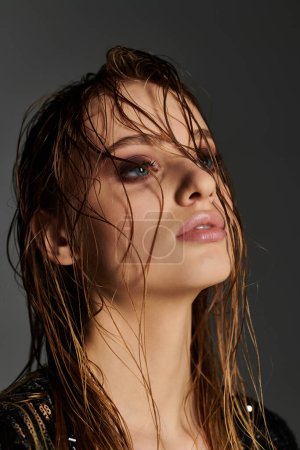 A young woman with wet hair standing against a gray background.