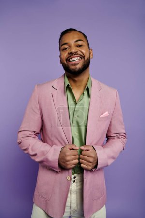 Téléchargez les photos : Un jeune homme élégant avec des bretelles sourit, vêtu d'une veste rose et d'une chemise verte sur un fond violet vif. - en image libre de droit