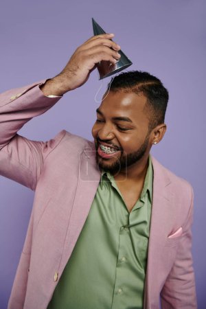 Photo for A happy, young African American man confidently poses in a pink suit and green shirt against a purple background. - Royalty Free Image