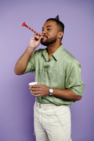 Ein fröhlicher junger afroamerikanischer Mann mit Geburtstagshut bläst Party-Horn vor violettem Hintergrund.