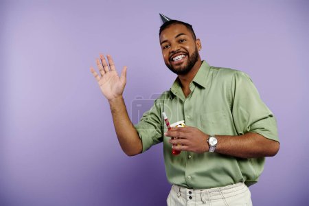 Young African American man with braces happily raises his hand on a purple background.