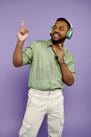 Téléchargez les photos : Un jeune Afro-Américain avec des bretelles pointe joyeusement sur le côté tout en portant un casque sur un fond violet. - en image libre de droit