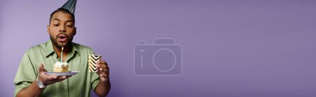 Foto de Un joven afroamericano soplando velas sobre un fondo púrpura. - Imagen libre de derechos