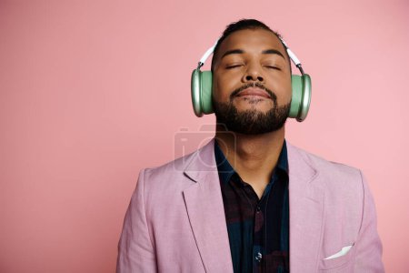 Un joven afroamericano escuchando música a través de auriculares sobre un fondo rosa.