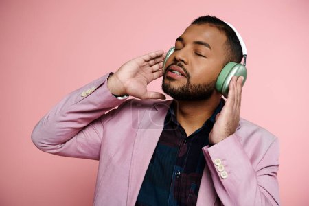 joven hombre afroamericano con aparatos ortopédicos escuchando auriculares con una elegante chaqueta rosa.