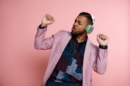 Foto de Joven hombre afroamericano con una chaqueta rosa y escuchando música en los auriculares. - Imagen libre de derechos