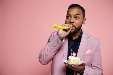 Ein stilvoller junger afroamerikanischer Mann im rosafarbenen Anzug genießt fröhlich ein Stück Kuchen auf einem leuchtend rosa Hintergrund.