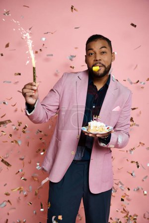 Young African American man in pink jacket joyfully holds a cake and sparkler in a celebratory moment.