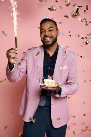 Foto de Young African American man in a pink jacket holds a sparkler on a vibrant pink background, expressing happiness. - Imagen libre de derechos