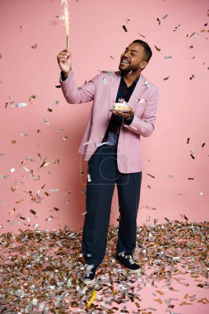 Téléchargez les photos : Lumineux scintillant tenu par un jeune homme afro-américain heureux dans une veste rose sur un fond vibrant. - en image libre de droit