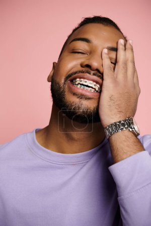 A young African American man smiling brightly, showcasing his braces, against a vibrant pink background.