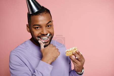 A young, happy African American man in braces smiling while indulging in a piece of cake at a celebration.