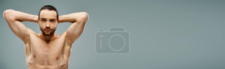 Photo for A shirtless man with a beard reclines with his hands behind his head in a serene pose on a grey background in a studio. - Royalty Free Image