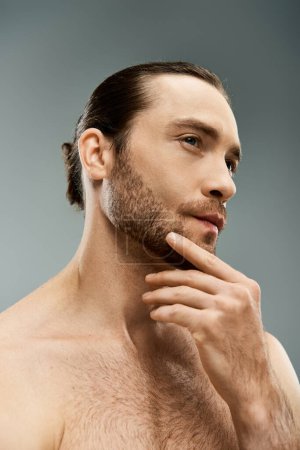 Foto de Un hombre sin camisa con una perilla impactante posa con confianza sobre un fondo gris del estudio. - Imagen libre de derechos