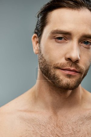 Handsome shirtless man with a beard striking a pose on a grey background in a studio setting.