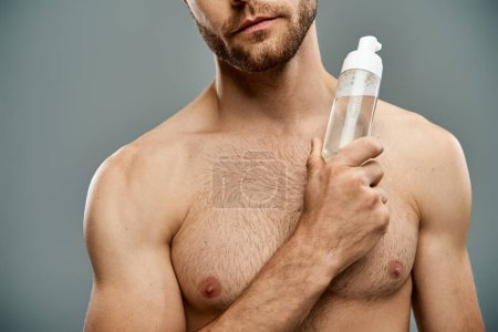 Photo for A handsome, shirtless man with a beard holds a bottle of facial cleanser - Royalty Free Image