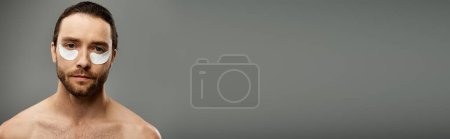 Téléchargez les photos : Un homme torse nu et barbu porte des bandeaux sur fond de studio gris. - en image libre de droit