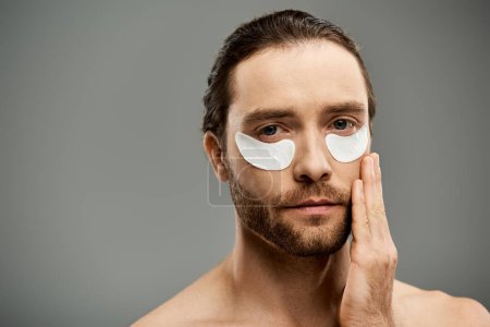 Téléchargez les photos : Un homme beau et torse nu avec une barbe portant des bandeaux sur le visage dans un studio sur fond gris. - en image libre de droit