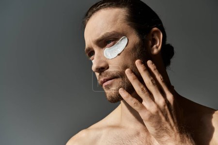 Foto de Un hombre sin camisa y barbudo muestra manchas en su cara en un fondo gris del estudio. - Imagen libre de derechos