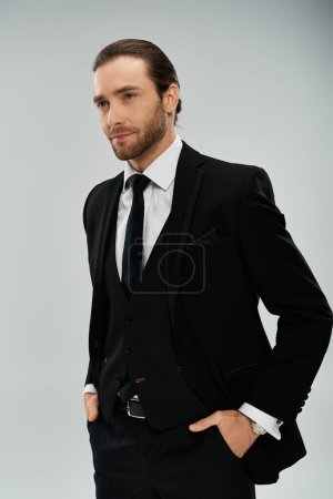 A bearded businessman exudes confidence while posing for a portrait in a sleek suit and tie on a neutral grey background.