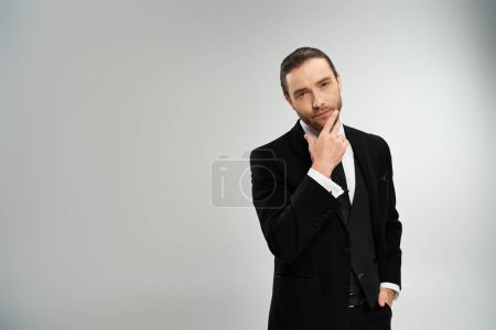 A handsome, bearded businessman in a suit strikes a pose against a grey background in a studio setting.