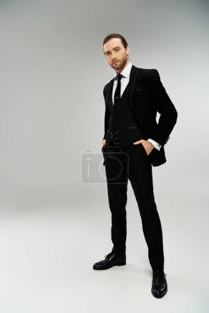 Téléchargez les photos : Un homme d'affaires barbu dans un smoking élégant pose en toute confiance sur un fond de studio gris. - en image libre de droit