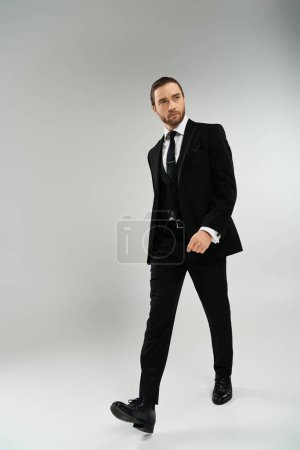 Téléchargez les photos : Un homme d'affaires barbu marche en toute confiance dans un costume et cravate sur fond de studio gris. - en image libre de droit