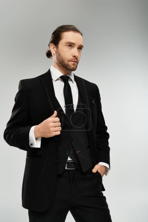 Foto de Un hombre de negocios barbudo y guapo con traje y corbata posa con confianza sobre un fondo gris de estudio. - Imagen libre de derechos