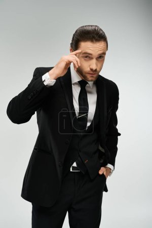 A handsome, bearded businessman in a suit holds his hand to his ear, listening intently. Studio shot on a grey background.